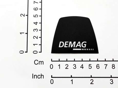 Aufkleber · Aufkleberbeschriftung: „Demag“, Aufkleberbreite: 62,2mm, Aufkleberhöhe: 49,8mm, Textfarbe: Weißer Text/Logo auf schwarzem Hintergrund Demag Identnummer D0003527